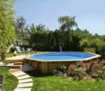 piscina de madera GoForPool, con diseño octogonal, semienterrada en un jardín con terraza en tarima de madera