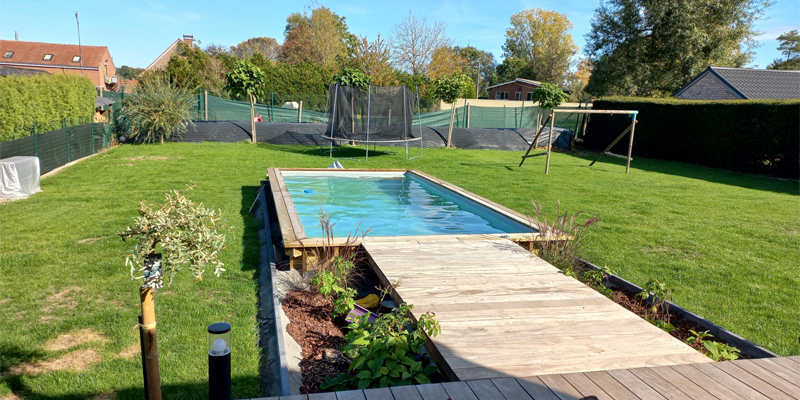piscina de madera, de GoForPool, con diseño rectangular, enterrada en un jardín con un pasillo de acceso también de madera